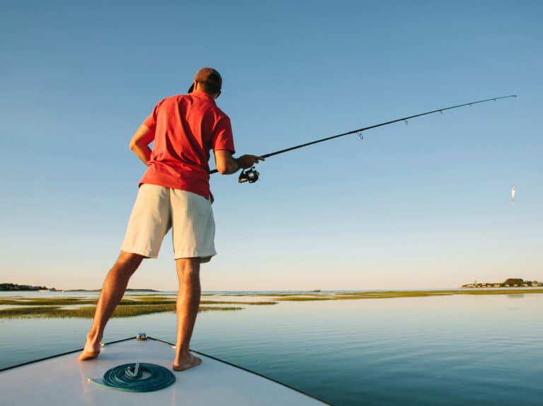 Man in summer clothes holds a fishing rod standing near the water